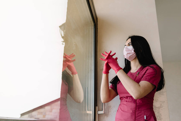 Портрет красивой медсестры или врача в маске со шприцем в руке, стоящим у окна в заброшенной медицинской клинике или лечебнице - Фото, изображение