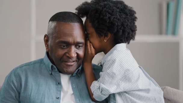 Afro-Amerikaanse dochter fluistert geheim volwassen vader in oor vertelt roddel verrast vader luistert goed vertrouwelijke informatie maken gebaar stilte geheim zet wijsvinger op mond - Video