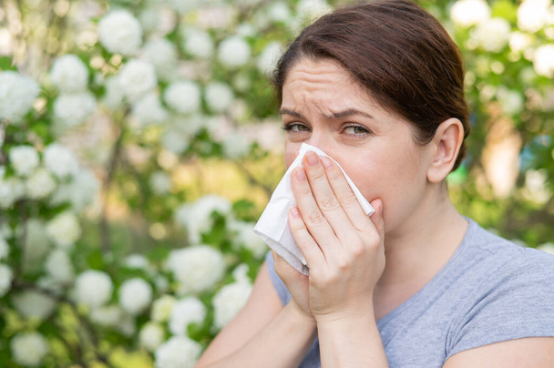 Caucasian woman suffers from allergies and sneezes while walking in the park - Foto, imagen