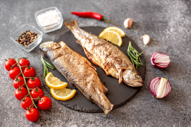 grilled trout fish with vegetables and spices on black stone background - Photo, Image