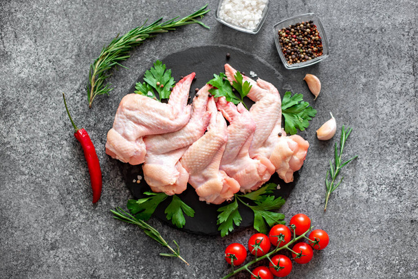 alitas de pollo crudas con ingredientes sobre fondo negro - Foto, Imagen