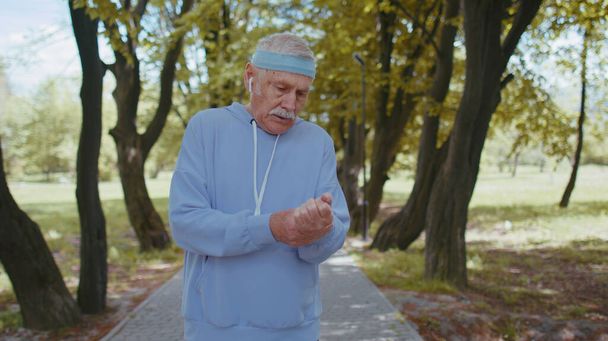 Elokuva motivoituneesta urheilukuntoilusta eläköitynyt aikuinen lenkkeilijä urheiluvaatteissa juoksemassa tarkistamassa pulssia kädessä puistossa. Aktiivinen vanhusten isoisä mies nauttii terveellistä urheilua elämäntapa - Valokuva, kuva