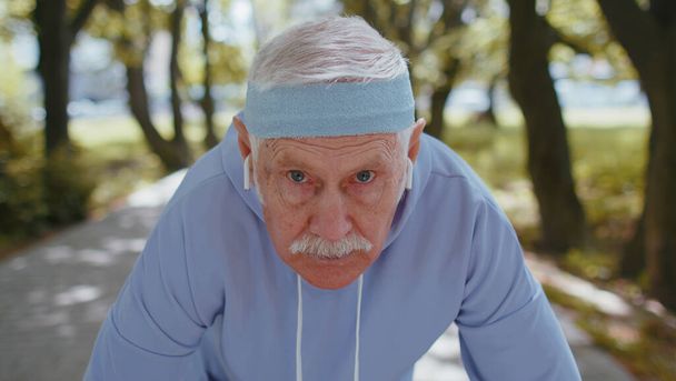 Atletische fitness senior man start race in het zonnige park. Actieve oudere grootvader joggen in de zomer bos tijdens de ochtend workout buiten. Actief pensioen, sport gezonde levensstijl concept - Foto, afbeelding