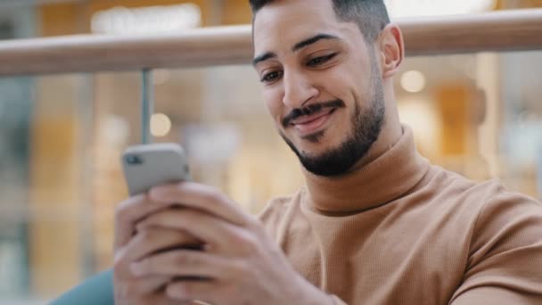 Yakın plan genç Arap adam elinde telefonla ekrandaki akıllı telefona bakıyor gülümsüyor güzel e-posta mesajları alıyor arkadaşlık sitelerinde geziniyor sosyal ağ ücretsiz kablosuz internetin keyfini çıkarıyor çevrimiçi mağazada siparişi onaylıyor - Video, Çekim
