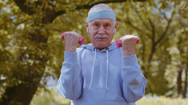 Alkalmasság időseknek. Erős idős ember gyakorolja a súlyemelő gyakorlatok készítését, sportedzést gyakorol a parkban. Aktív nyugdíjas felnőtt emberek. Nagyapa élvezi az egészséges életmódot - Fotó, kép