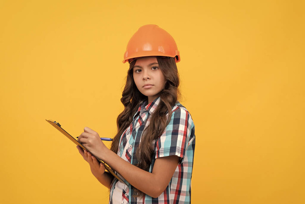 construction documents. signing a contract. on construction site. future engineer hold clipboard. safety work expertise. teen girl in protective hard hat making notes. child in helmet read project. - Photo, Image