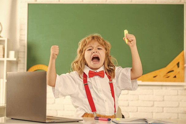 schreeuwende jongen jongen in strikje studeren in school klaslokaal op schoolbord, emoties. - Foto, afbeelding