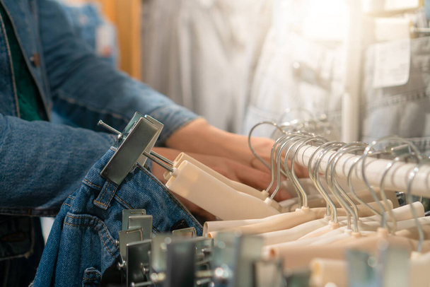 Lähikuva naisen käsi menee läpi ripustimet farkut myymälässä, valikoiva keskittyä. Naisten vaatteet ripustimet, valikoima housuja putiikissa, uusi kokoelma farkkuja - Valokuva, kuva