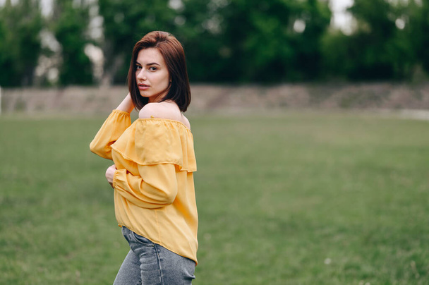 Chica posando sobre un fondo veraniego. Una joven con una blusa amarilla. El concepto de un fin de semana en la naturaleza. - Foto, imagen