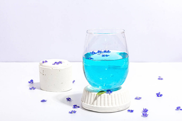Koud tonic water en blauw vergeet me niet bloemen op staan geïsoleerd op een witte achtergrond. Voorjaarsconcept, bloemenelement, een hard licht, donkere schaduw, selectieve focus, close-up - Foto, afbeelding