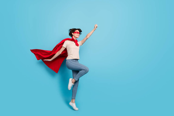 Full length photo of lucky cool woman wear red cape jumping rising fist empty space isolated blue color background. - Foto, Imagen