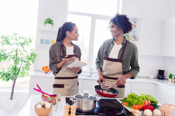Photo of two cheerful positive tv show colleagues prepare food write recipe speak communicate kitchen indoors. - Φωτογραφία, εικόνα