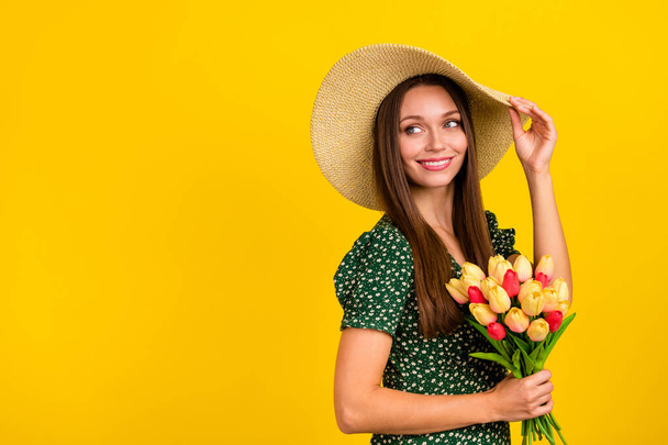 Profile photo of cute stunning lady touch sunhat hold flowers look empty space toothy smile isolated on yellow color background. - Foto, afbeelding