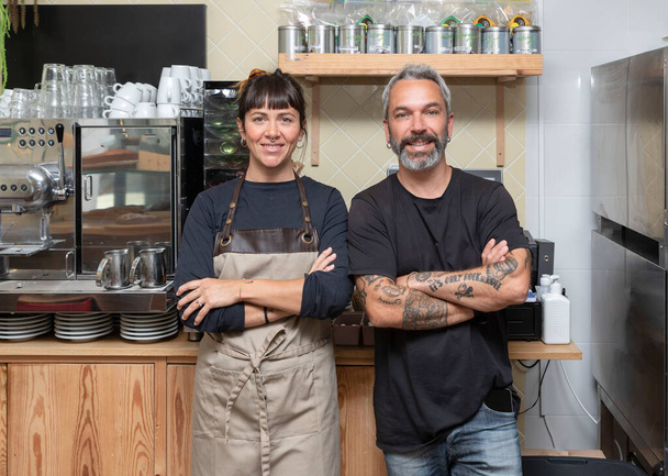 Boldog tulajdonos és egy pincérnő egy kávézó pult mögött keresztbe tett karokkal, a kamerába nézve.. - Fotó, kép