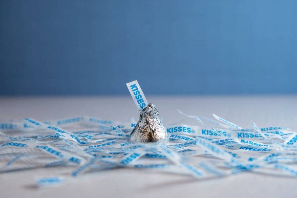 Flourtown, PA - 28 Mayıs 2022: Tek bir Hershey 's Kiss çikolataların yuvasına oturmuş mavi ve beyaz bir arka planı var. Kağıt etikete bir tüy ya da bazen bir "Zenci Wiggly" denir.." - Fotoğraf, Görsel