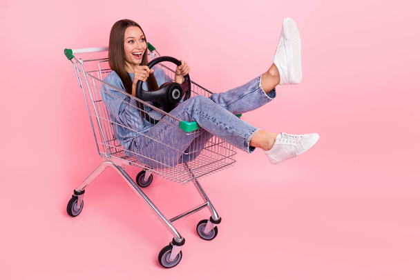 Full length body size view of attractive cheery girl sitting in cart holding steering wheel isolated over pink pastel color background. - 写真・画像