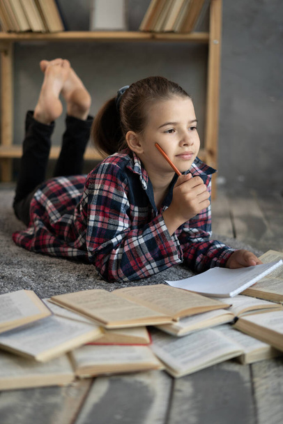 smiling little student girl with book lying on the floor, education and school concept - 写真・画像