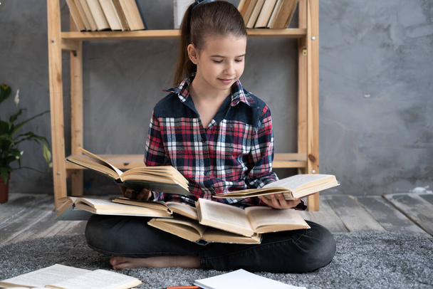 iskolás lány ül a padlón, és iskolai feladatokat végez egy halom könyvvel körülvéve, gyerek könyvet olvas otthon. oktatás és iskolai koncepció. - Fotó, kép