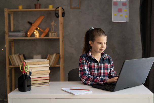 boldog lány iskolás lány gépel laptopon és házi feladatot csinál otthon. emberek, gyermekek, oktatás és tanulás koncepciója - Fotó, kép