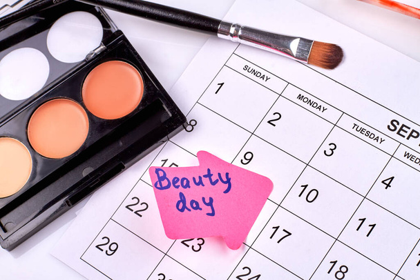 Concepto del día de belleza. Polvo cosmético con pincel y calendario. Maquillaje accesorios cosméticos. - Foto, Imagen