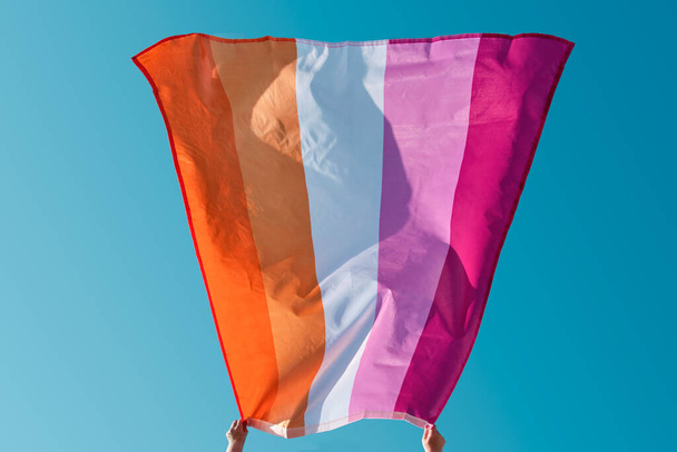 Valkoihoinen nainen pitelee lesbo ylpeys lippua ilmassa taivasta vasten aurinkoisena päivänä - Valokuva, kuva