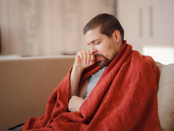 Coronavirus. Sick man of corona virus lying down in sofa and recovery from illness in home. Blowing his nose. The concept of high temperatures. The person is seriously ill. - Photo, Image