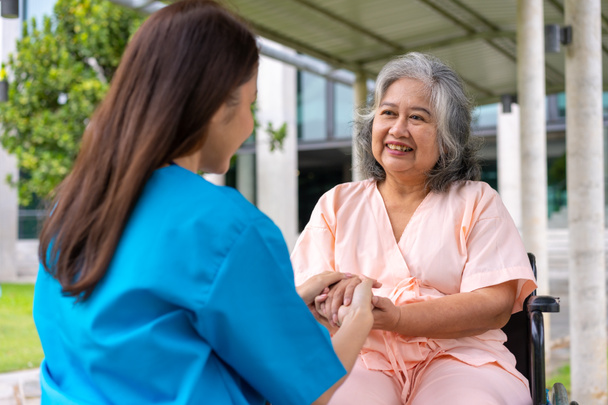 Azjatycki ostrożny opiekun lub pielęgniarka trzymać pacjenta za rękę i zachęcać pacjenta na wózku inwalidzkim. Koncepcja szczęśliwej emerytury z opieką opiekuna i Oszczędności i starszego ubezpieczenia zdrowotnego. - Zdjęcie, obraz