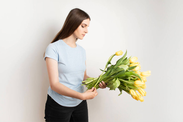 Mujer feliz sostiene tulipanes amarillos en sus manos. La florista reunió un ramo. Pétalo de flor. Foto de alta calidad - Foto, Imagen