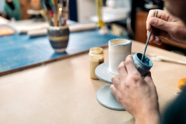 Stock photo of unrecognized person using paintbrush during pottery class. - Foto, Imagen