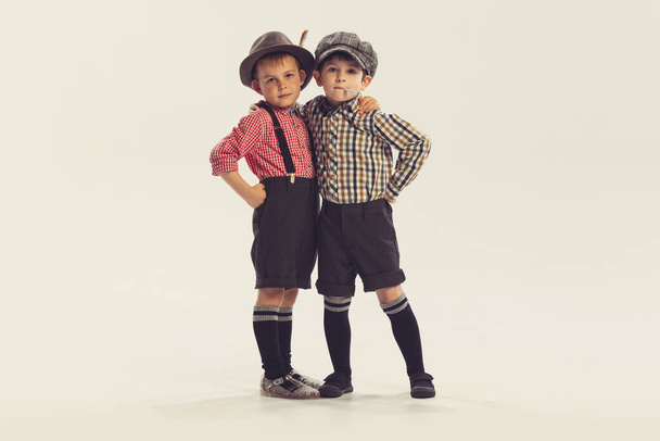 Huggs. Portrait of two little boys, children in retro style clothes posing, looking at camera isolated over grey studio background. Concept of childhood, friendship, family, fun, lifestyle, fashion - Fotoğraf, Görsel