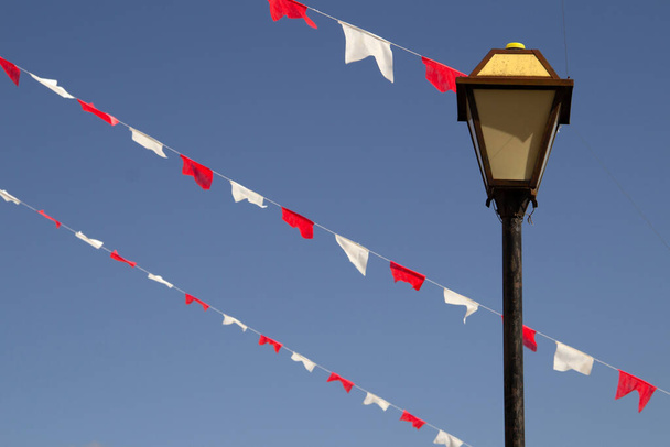 Arka planda mavi gökyüzü olan beyaz ve kırmızı bayraklı bir sokak lambası. Lamba direği. Bayraklı lamba. - Fotoğraf, Görsel