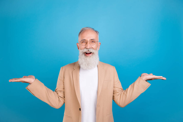 Retrato de anciano jubilado jubilado guapo alegre hombre de pelo gris sosteniendo en el espacio de copia de la palma aislado sobre fondo de color azul brillante. - Foto, Imagen