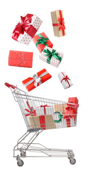 Beautifully wrapped gift boxes falling into metal shopping cart on white background - Fotó, kép