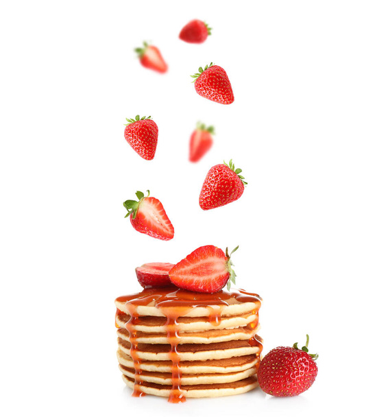 Fresh strawberries falling onto stacked pancakes against white background - Фото, изображение