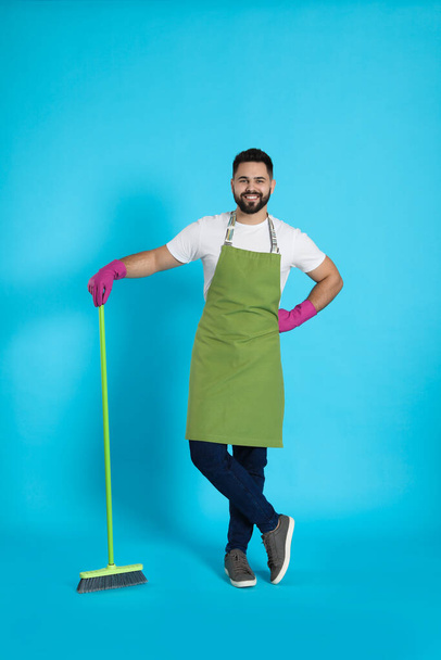Young man with green broom on light blue background - Foto, imagen