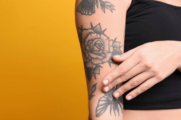 Woman with tattoos on arm against yellow background, closeup. Space for text - Fotoğraf, Görsel