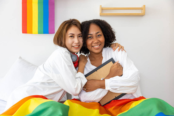 Couple of same sex marriage from difference races holding LGBTQ rainbow flag for pride month to promote equality and differences of homosexual and discrimination concept - Fotografie, Obrázek
