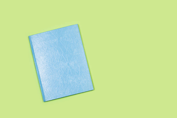 Een blauwe omslag gesloten boek op een groene achtergrond met kopieerruimte - Foto, afbeelding