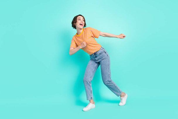 Photo of impressed funny young lady wear orange t-shirt dancing smiling isolated turquoise color background. - Fotografie, Obrázek
