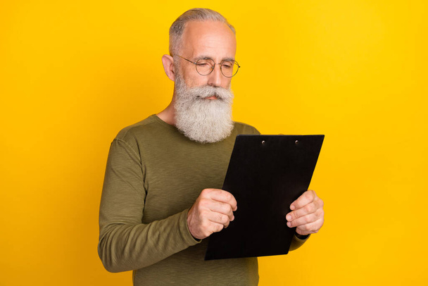 Foto de um agente de seguros sério barbudo homem ler prancheta usar óculos camisa verde isolado cor amarela fundo. - Foto, Imagem