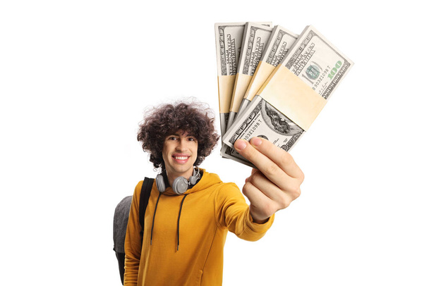 Cheerful male student carrying a backpack and showing stacks of money isolated on white background - Photo, image