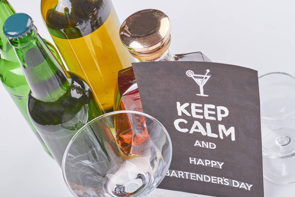 Mantenga la calma y feliz día de camareros. Muchas botellas de alcohol sobre fondo blanco. Vista superior bebidas alcohólicas. - Foto, Imagen