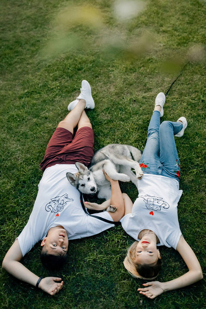 Vtipný hravý pes. Mladý milující a veselý pár v krásném parku. Pohled na řeku a bílý dům. Husky pes flákání kolem - Fotografie, Obrázek