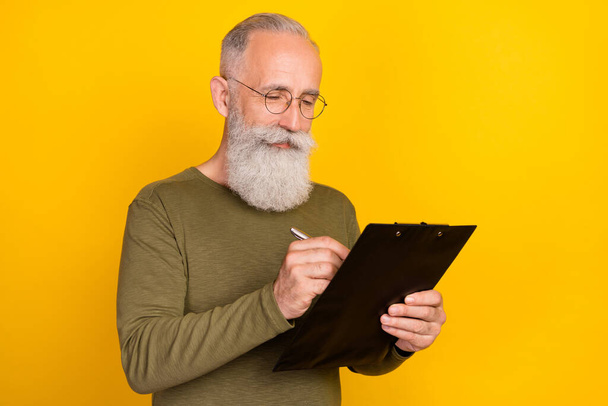 Photo of optimistic elder grey beard man write wear eyewear green sweater isolated on yellow color background. - 写真・画像