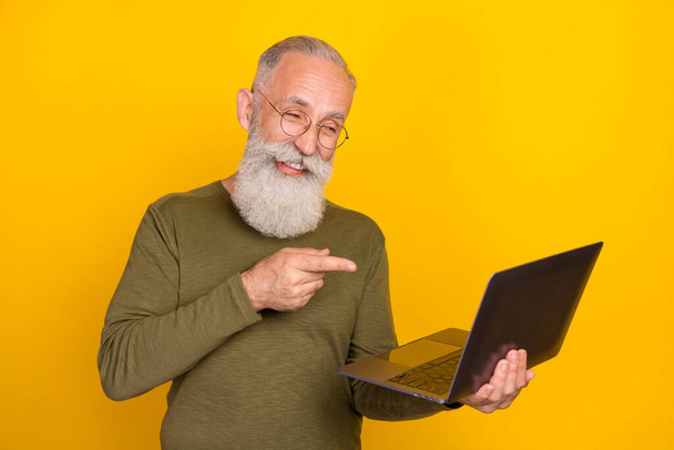 Photo of old man hold pc direct finger device wear spectacles green shirt isolated yellow color background. - Foto, immagini