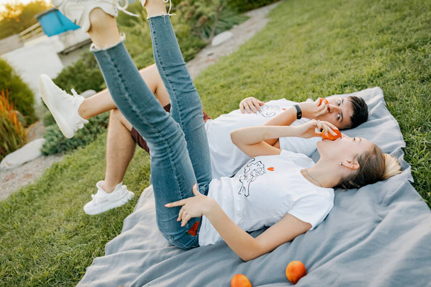 Ein junges fröhliches Paar verliebt und fröhlich in einem schönen Park auf einem Bett aus grünem Gras mit Früchten liegend. - Foto, Bild