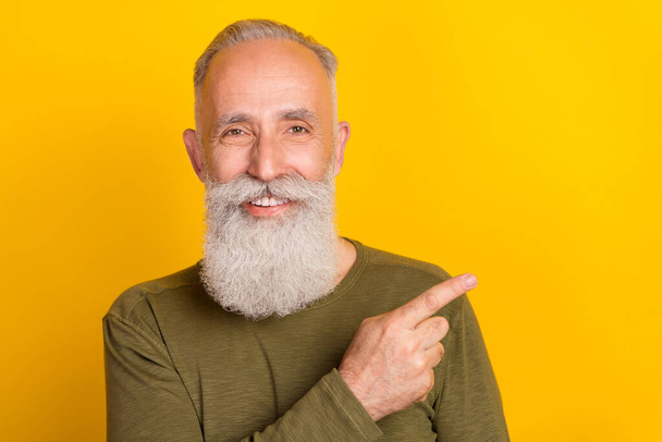 Photo of optimistic elder white beard man point empty space wear green sweater isolated on yellow color background. - Zdjęcie, obraz