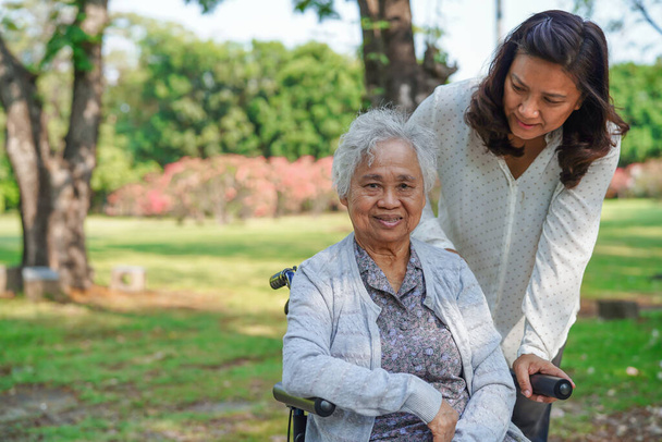 Φροντιστής βοήθεια και υποστήριξη ασιατική ανώτερος ή ηλικιωμένη ηλικιωμένη γυναίκα ασθενή σε αναπηρική καρέκλα στο πάρκο, υγιή ισχυρή ιατρική έννοια.  - Φωτογραφία, εικόνα