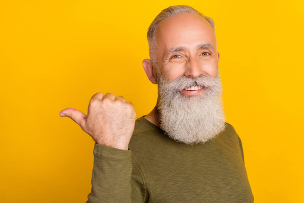 Photo of cheerful promoter grandpa direct finger empty space wear green shirt isolated yellow color background. - Foto, Imagen