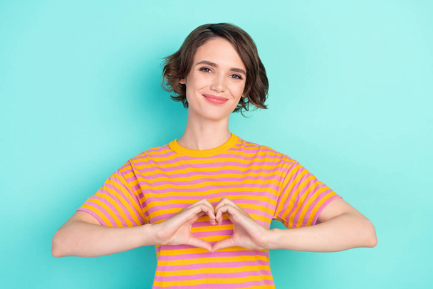 Photo of pretty shiny young lady wear orange t-shirt showing fingers heart isolated turquoise color background. - Foto, afbeelding